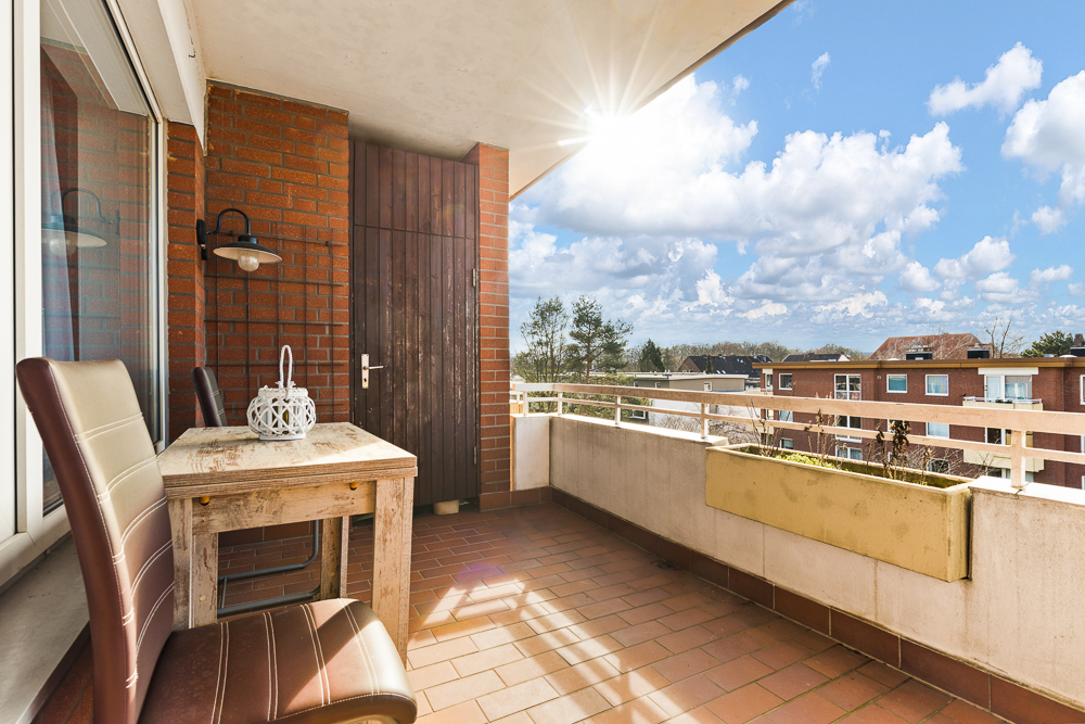 Heller Balkon mit zwei Stühlen, einem Holztisch und Blick auf Nachbargebäude.