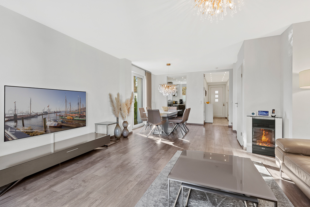Modernes Wohnzimmer mit Kamin, Fernseher, Esstisch und großen Fenstern.