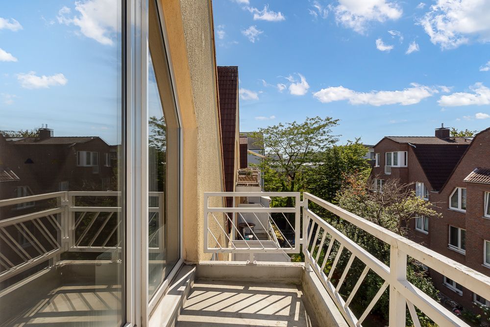 Kleiner Balkon mit Metallgeländer, Blick auf benachbarte Wohnhäuser und Bäume bei sonnigem Wetter.
