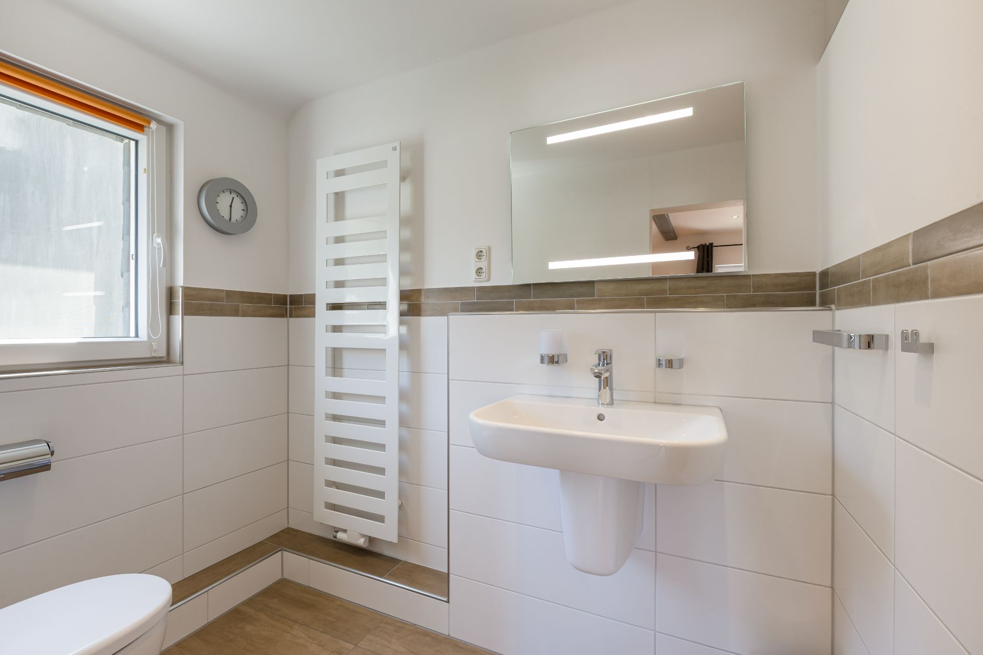 Modernes Badezimmer mit Fenster, Wandheizkörper, Spiegel und Waschbecken.