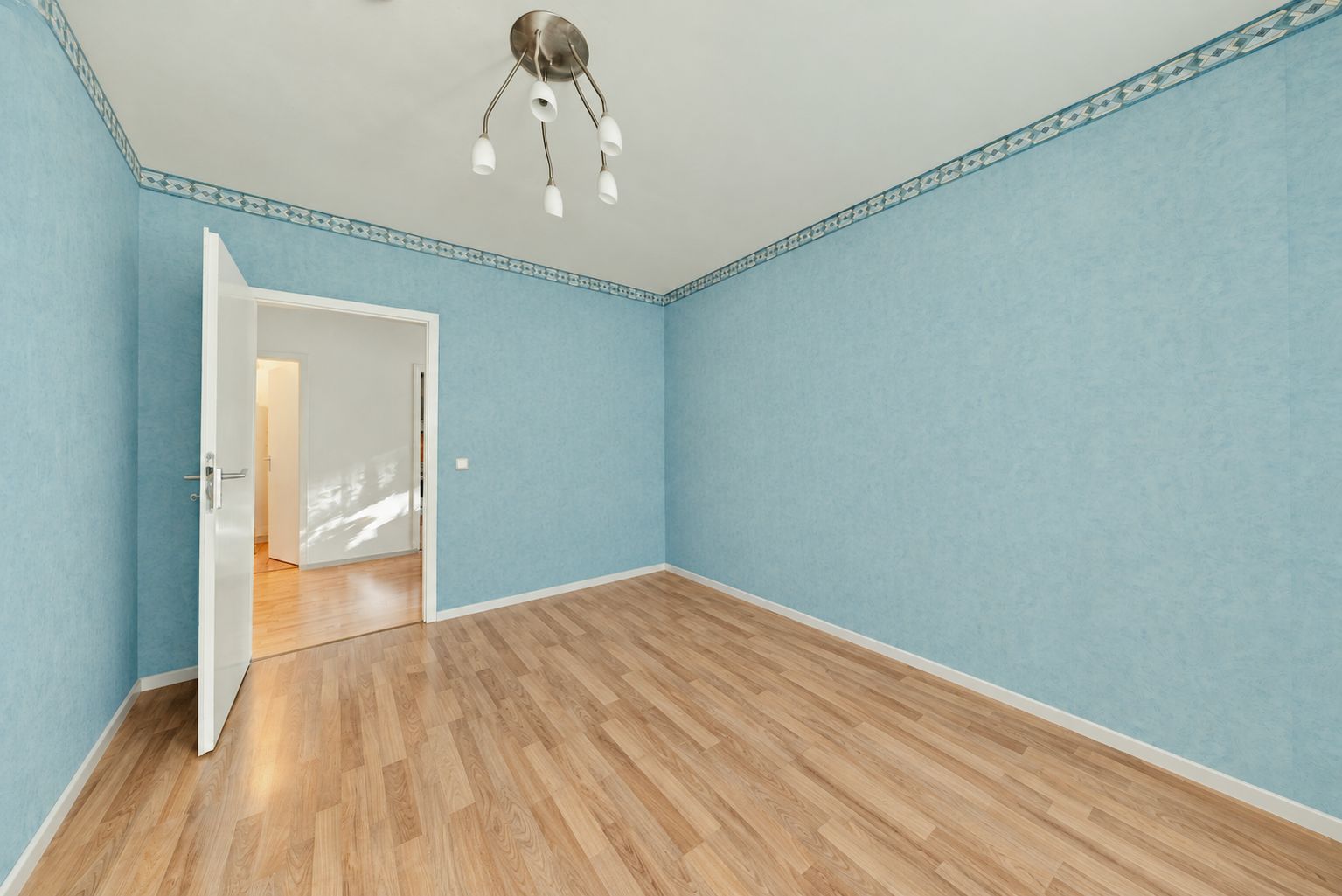 Leeres Zimmer mit blauen Wänden, Holzfußboden und Deckenlampe, offene Tür zum Flur.
