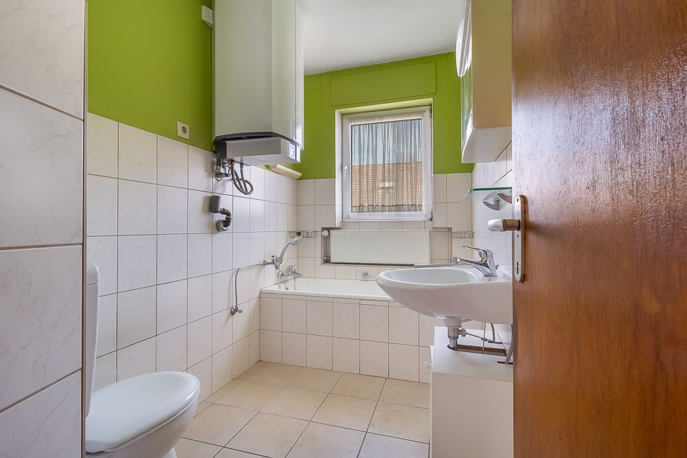 Helles Badezimmer mit Badewanne, Waschbecken, Toilette und Fenster, grüne Wand oben.