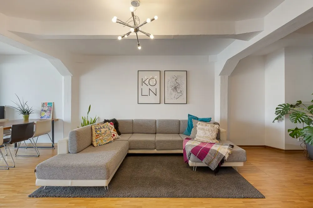 Modernes Wohnzimmer mit grauem Ecksofa, Teppich, Pflanzen und Wandbildern.