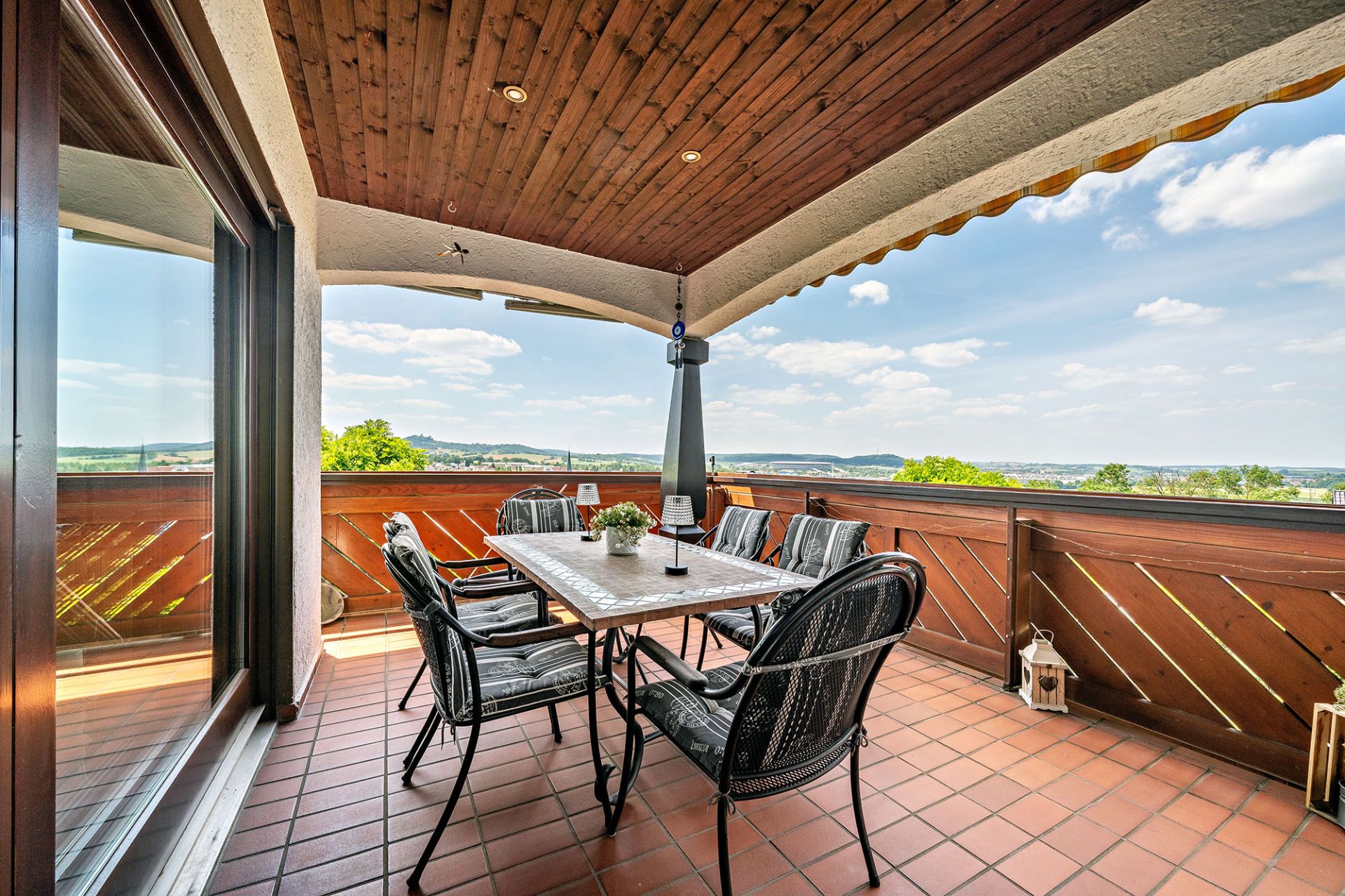 Überdachte Terrasse mit Esstisch und sechs Stühlen, Blick ins Grüne.