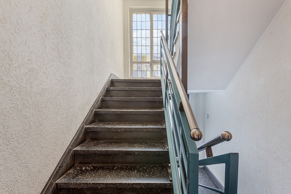 Treppe mit Metallgeländer und Fenster am oberen Ende in einem Wohnhaus.