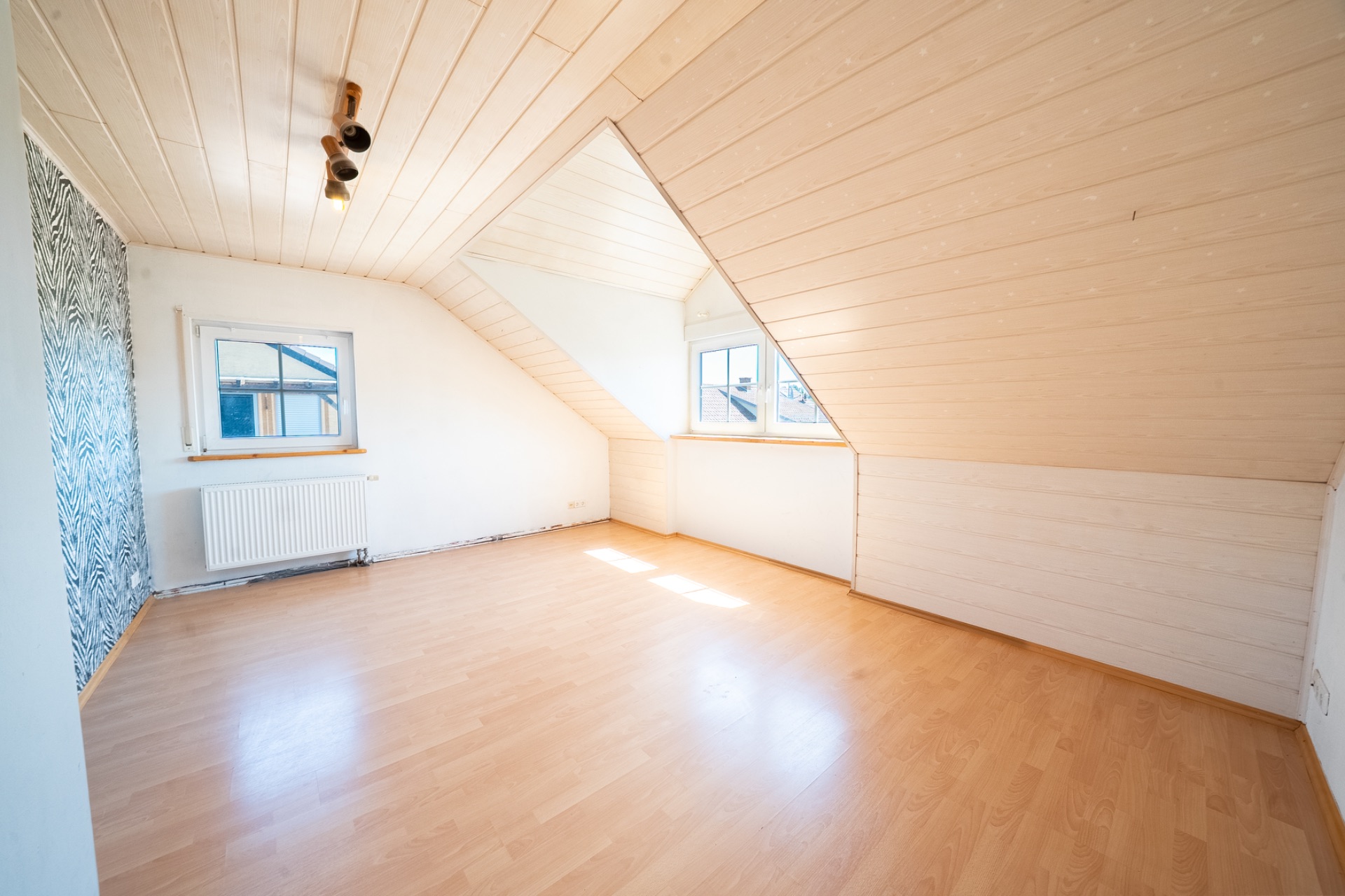 Heller Dachraum mit Holzdecke, zwei Fenstern und hellem Laminatboden.