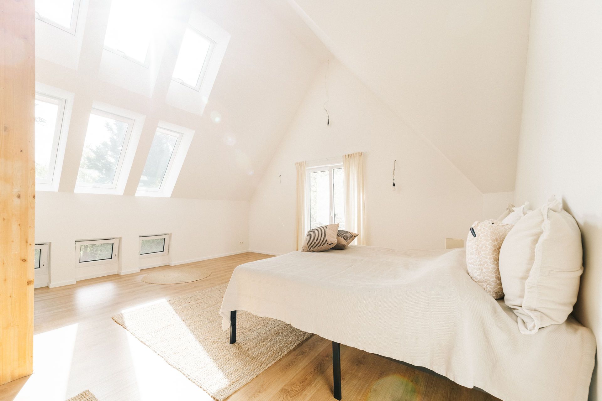 Helles Schlafzimmer mit Dachfenstern, Holzboden, Bett und Teppich.