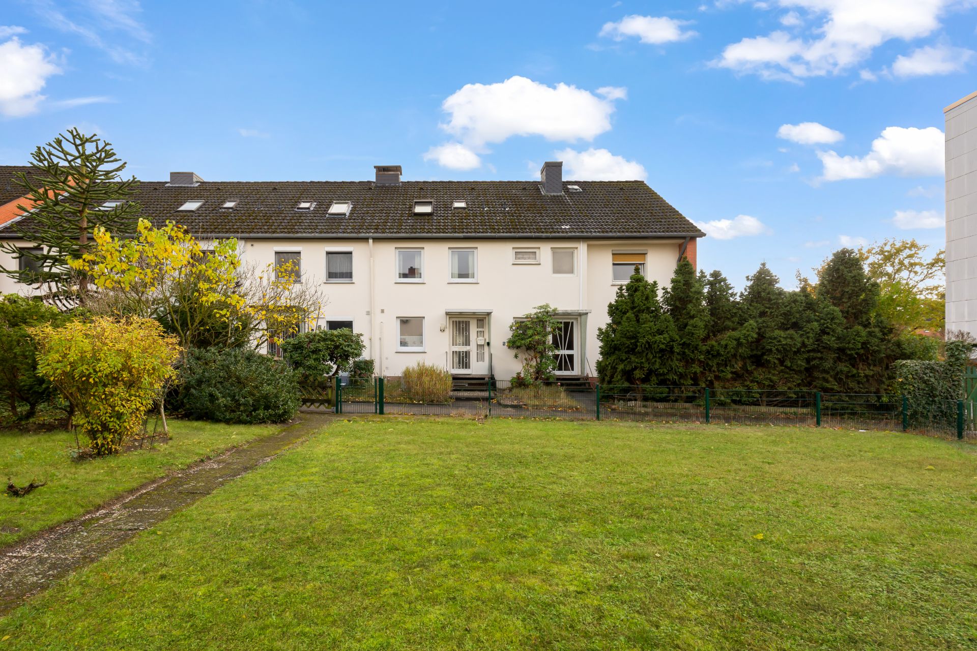 Rückansicht eines Reihenhauses mit Garten und Rasenfläche, umgeben von Büschen und Bäumen.