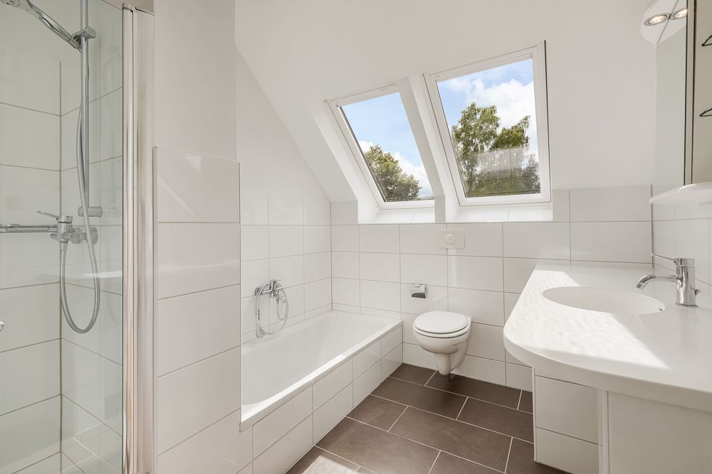 Modernes Badezimmer mit Badewanne, Dusche, WC, Waschbecken und zwei Dachfenstern.
