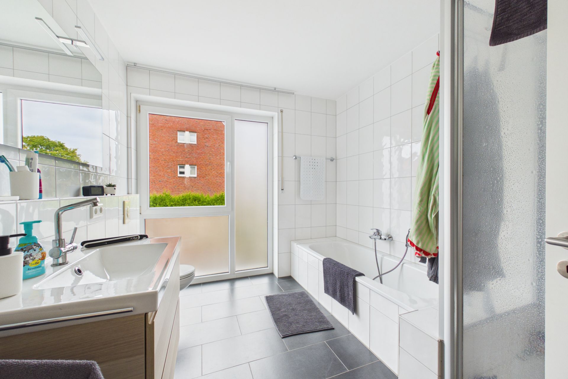 Modernes Badezimmer mit Badewanne, Dusche, Waschbecken und Fenster mit Blick nach draußen.