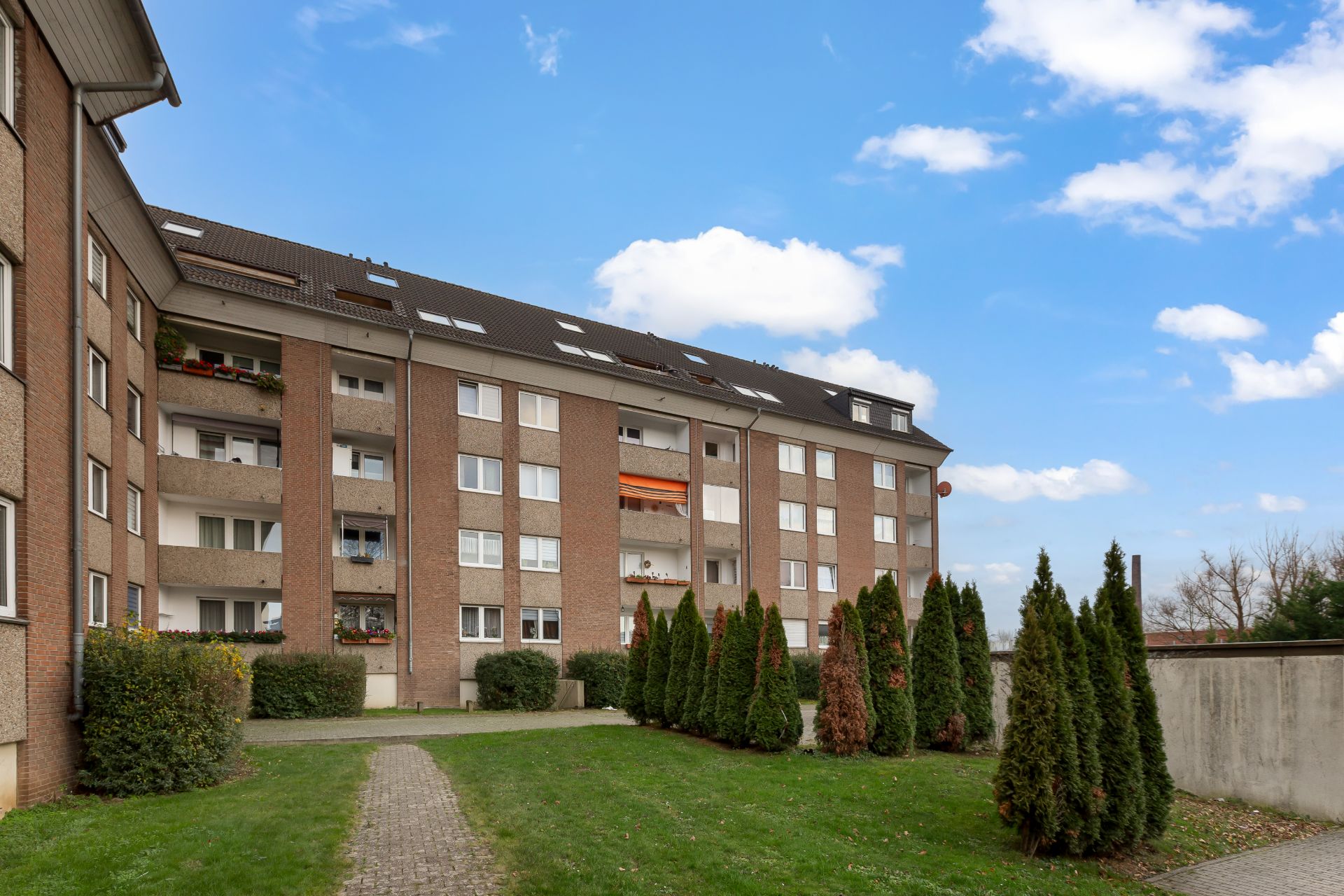 Mehrfamilienhaus mit Balkonen, kleiner Garten mit Weg und Sträuchern im Vordergrund.