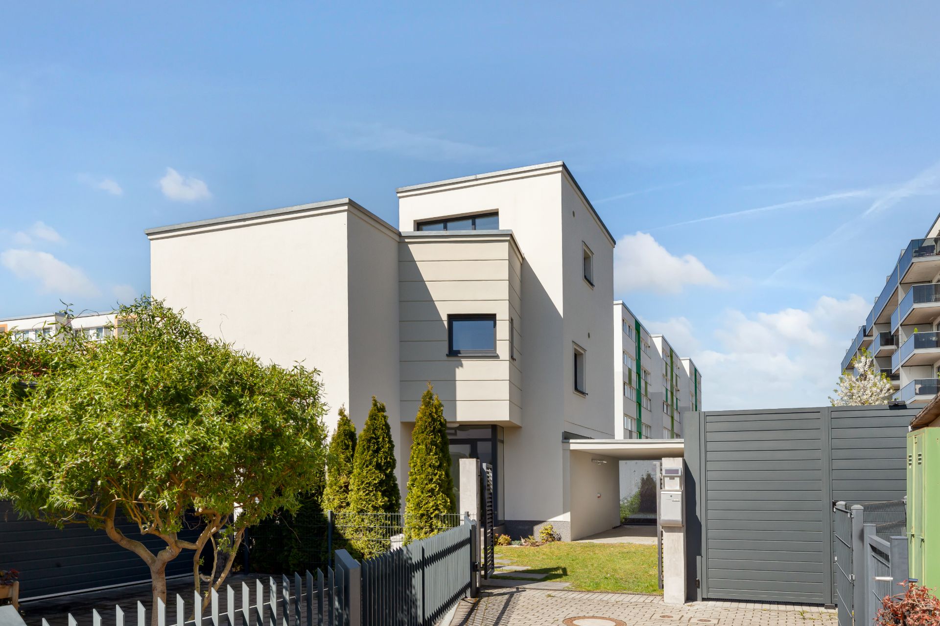 Modernes Wohnhaus mit flachem Dach, Garten und Einfahrt, umgeben von Zäunen und Bäumen.