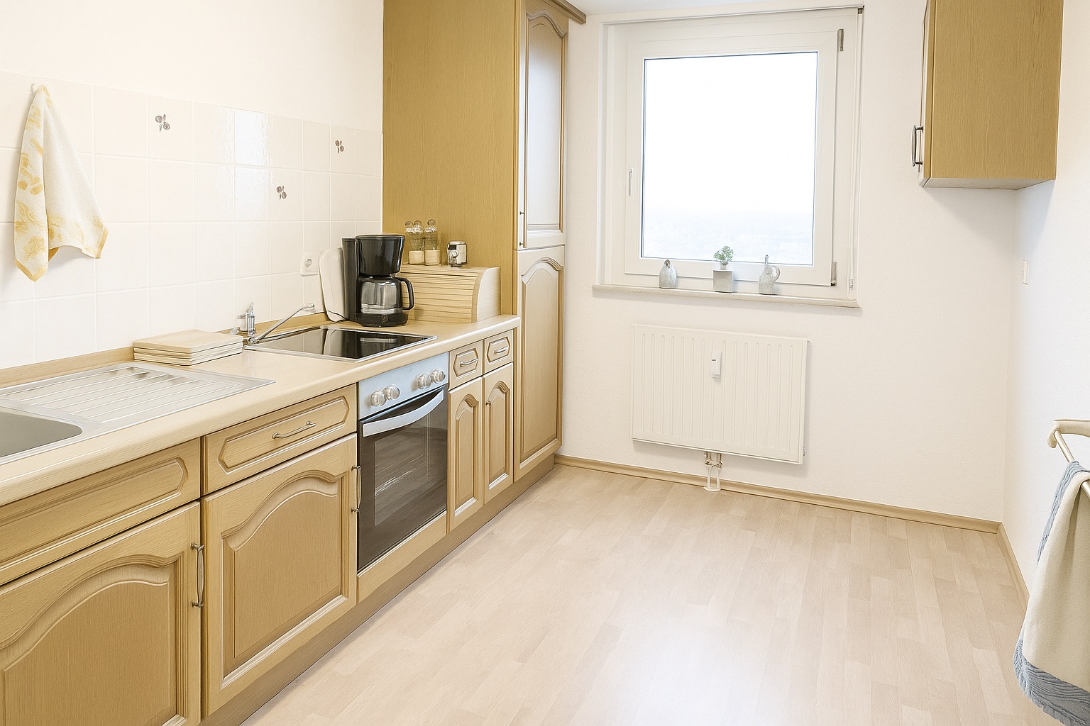 Helle Küche mit Holzschränken, Elektroherd, Spüle und Fenster mit drei kleinen Pflanzen.