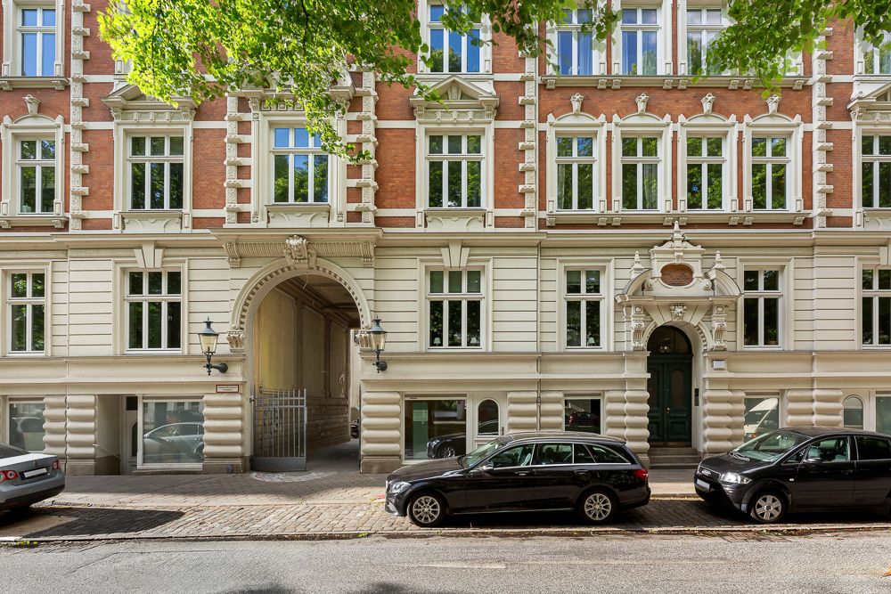 Fassade eines mehrstöckigen Wohnhauses mit vielen Fenstern und parkenden Autos davor.