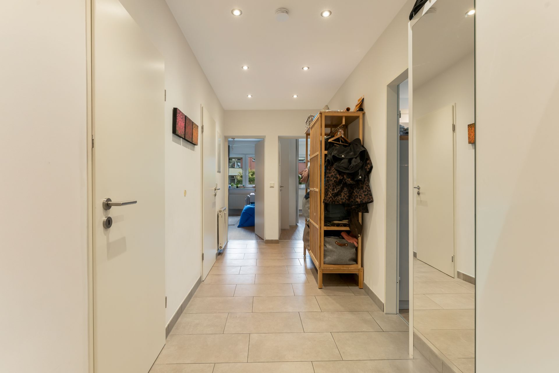 Heller Flur mit Fliesenboden, Garderobe und Spiegel an der Wand, Türen führen zu weiteren Räumen.