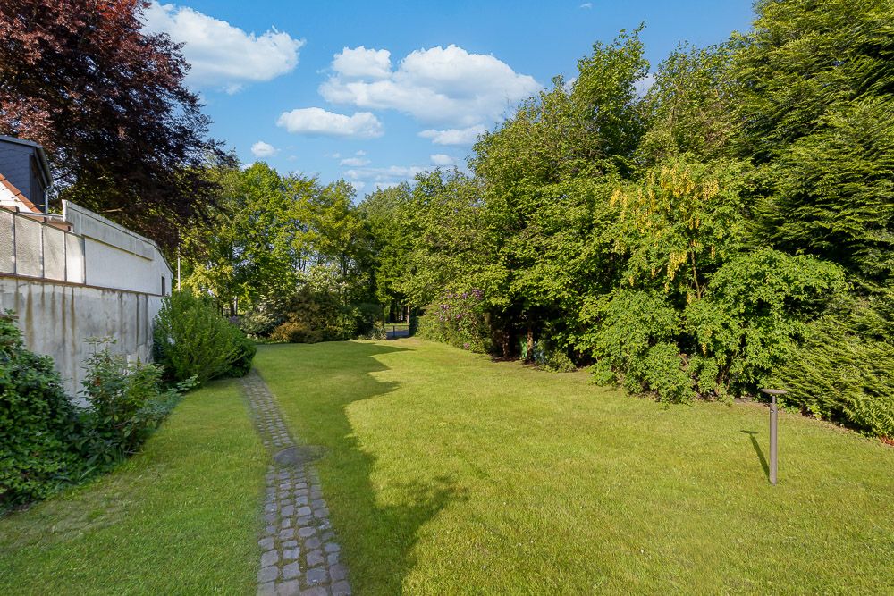 Garten mit Rasenfläche, Kopfsteinpflasterweg und Bäumen an den Seiten.