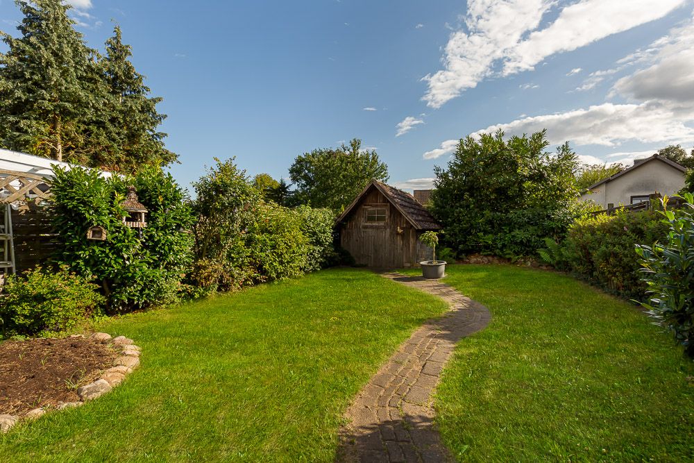Gepflegter Garten mit Rasen, Steinweg und einem kleinen Holzhaus im Hintergrund.