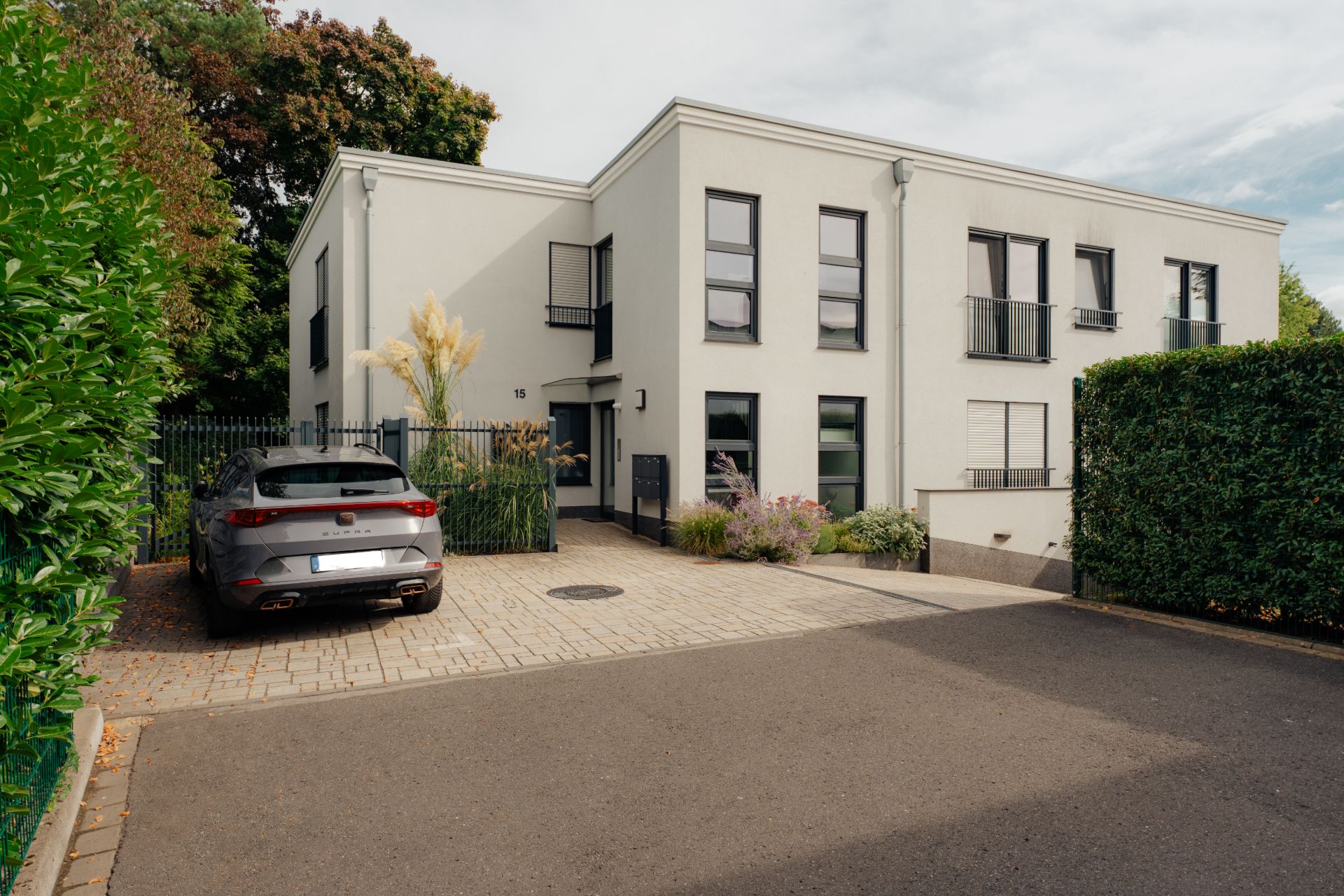 Modernes, zweistöckiges Wohnhaus mit großen Fenstern, Einfahrt und geparktem Auto davor.