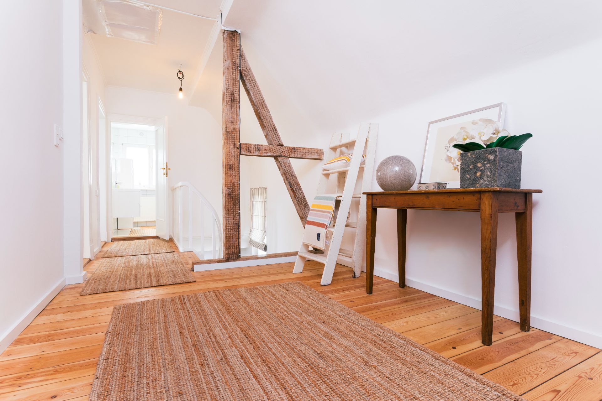 Heller Flur mit Holzfußboden, Teppichen, Holztisch und Regal mit Dekoration.