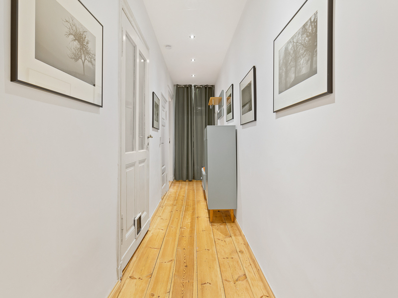 Heller Flur mit Holzboden, weißen Wänden, Bildern und einem Sideboard.