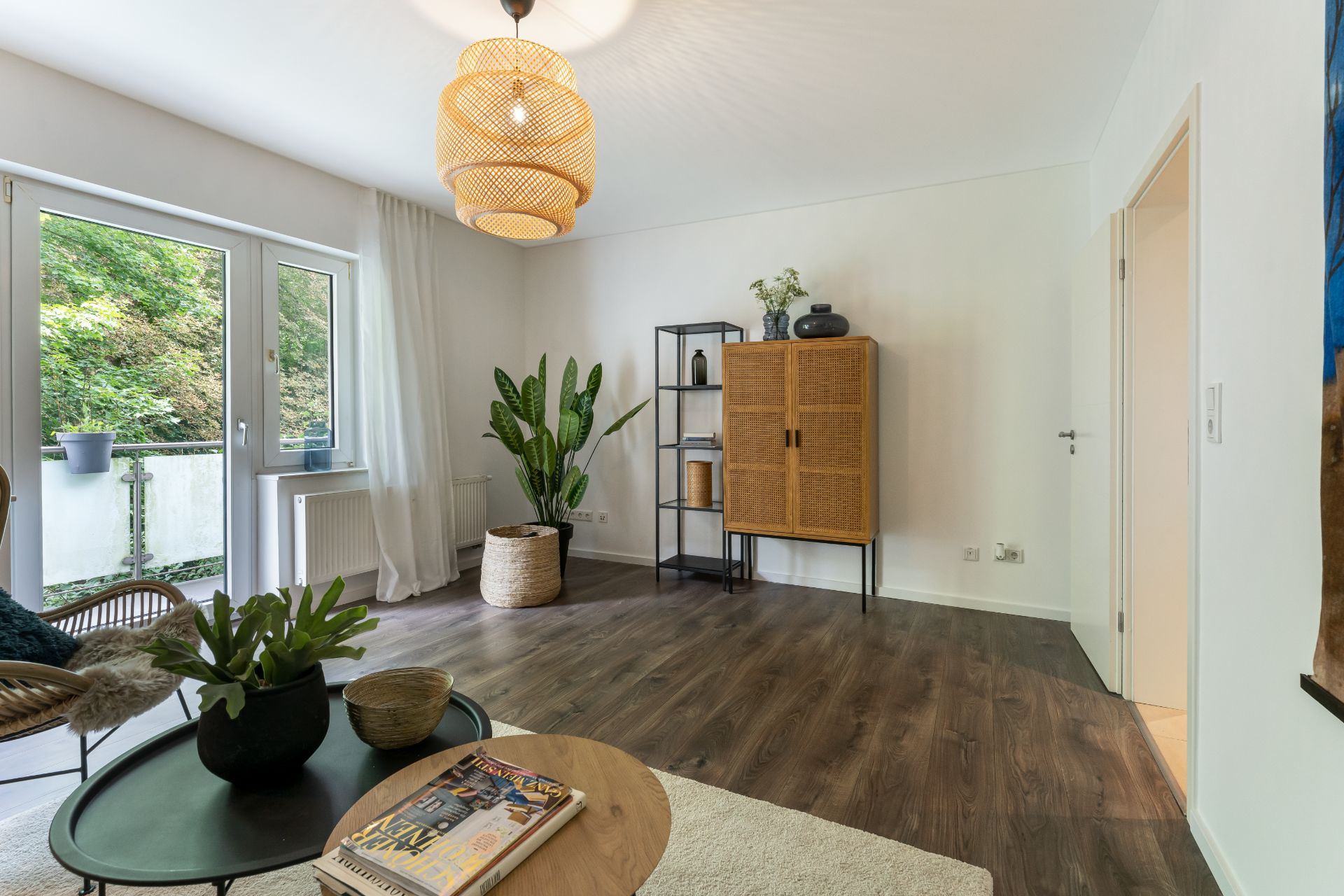 Helles Wohnzimmer mit Holzboden, großen Fenstern, Pflanzen und modernen Möbeln.