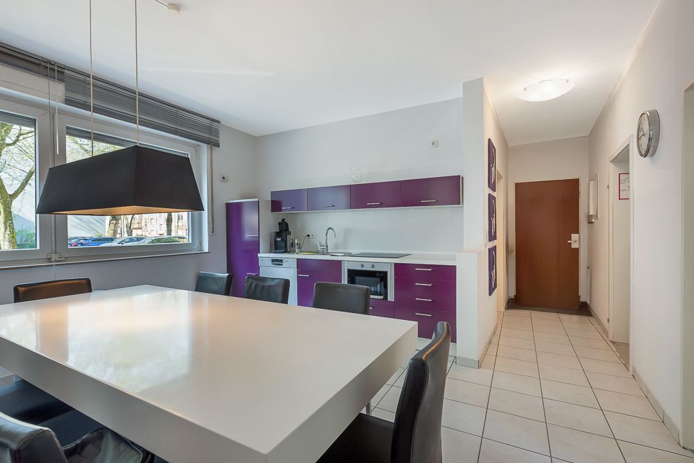 Moderne Küche mit lila Schränken, großem Esstisch und sechs Stühlen, Fenster mit Blick nach draußen.