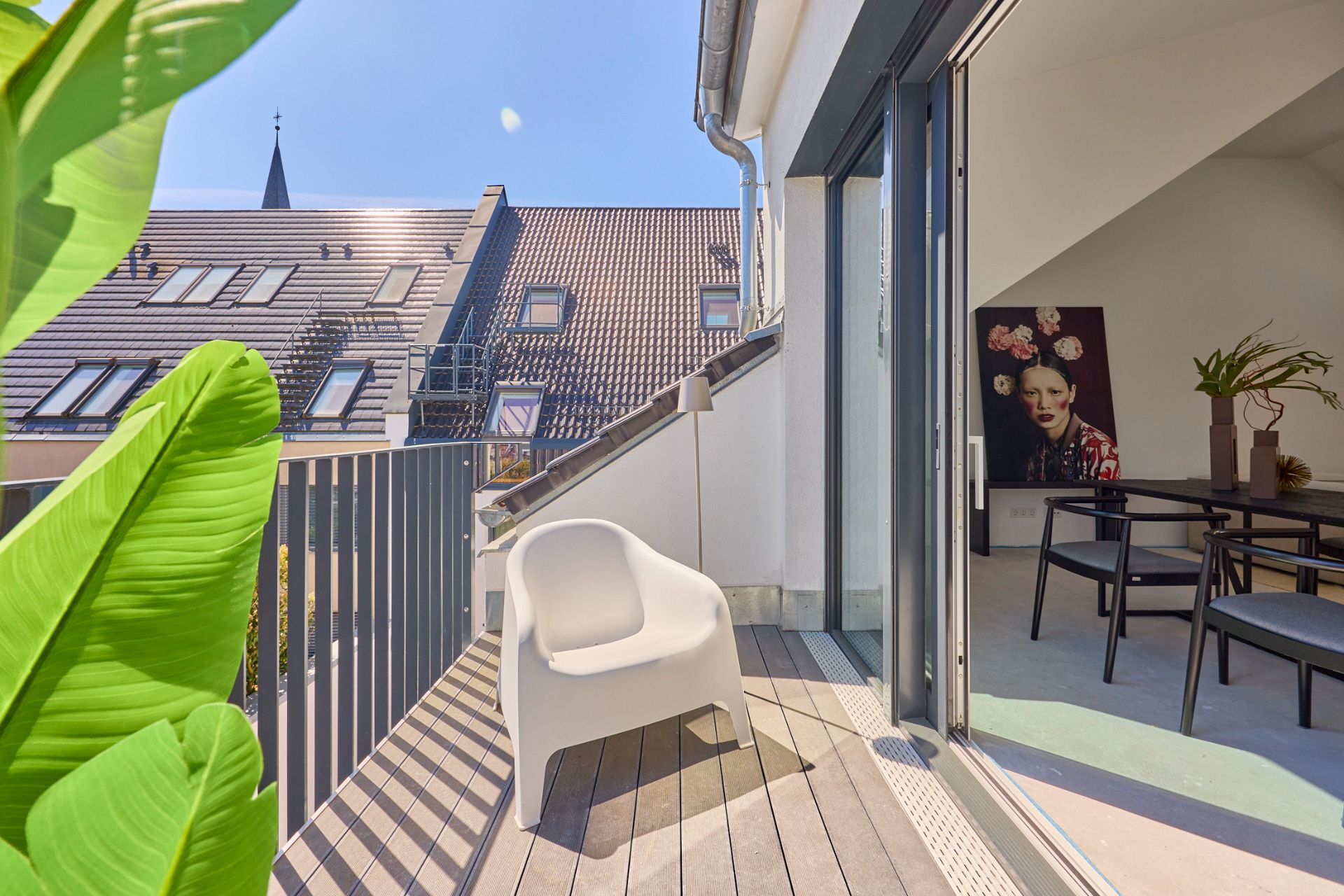 Balkon mit weißem Stuhl, Pflanze und Blick in ein Esszimmer mit Tisch und Stühlen.