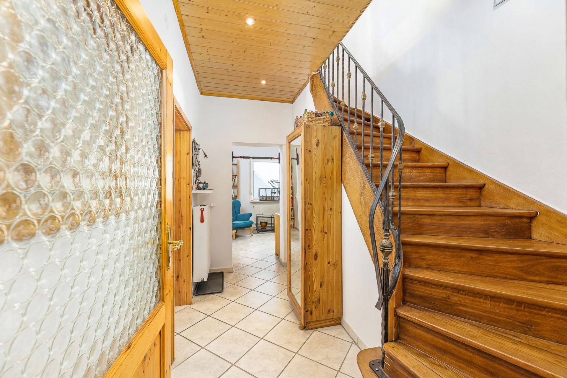 Flur mit Holztreppe, Fliesenboden und Holzdecke, Garderobe rechts, Tür mit Glas links.