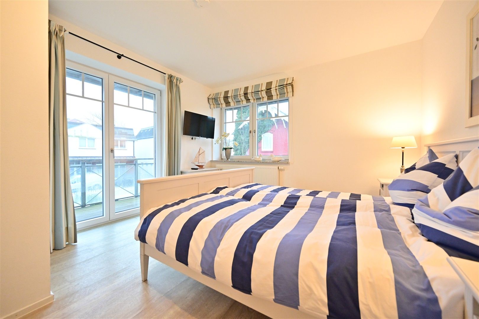 Helles Schlafzimmer mit Doppelbett, gestreifter Bettwäsche, großem Fenster und Glastür zum Balkon.