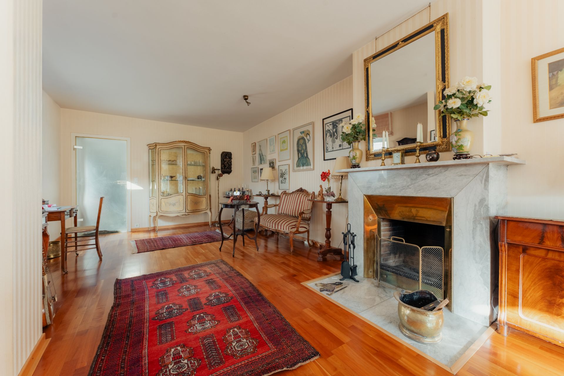 Wohnzimmer mit Kamin, Holzboden, roten Teppichen, antiken Möbeln und Bildern an der Wand.
