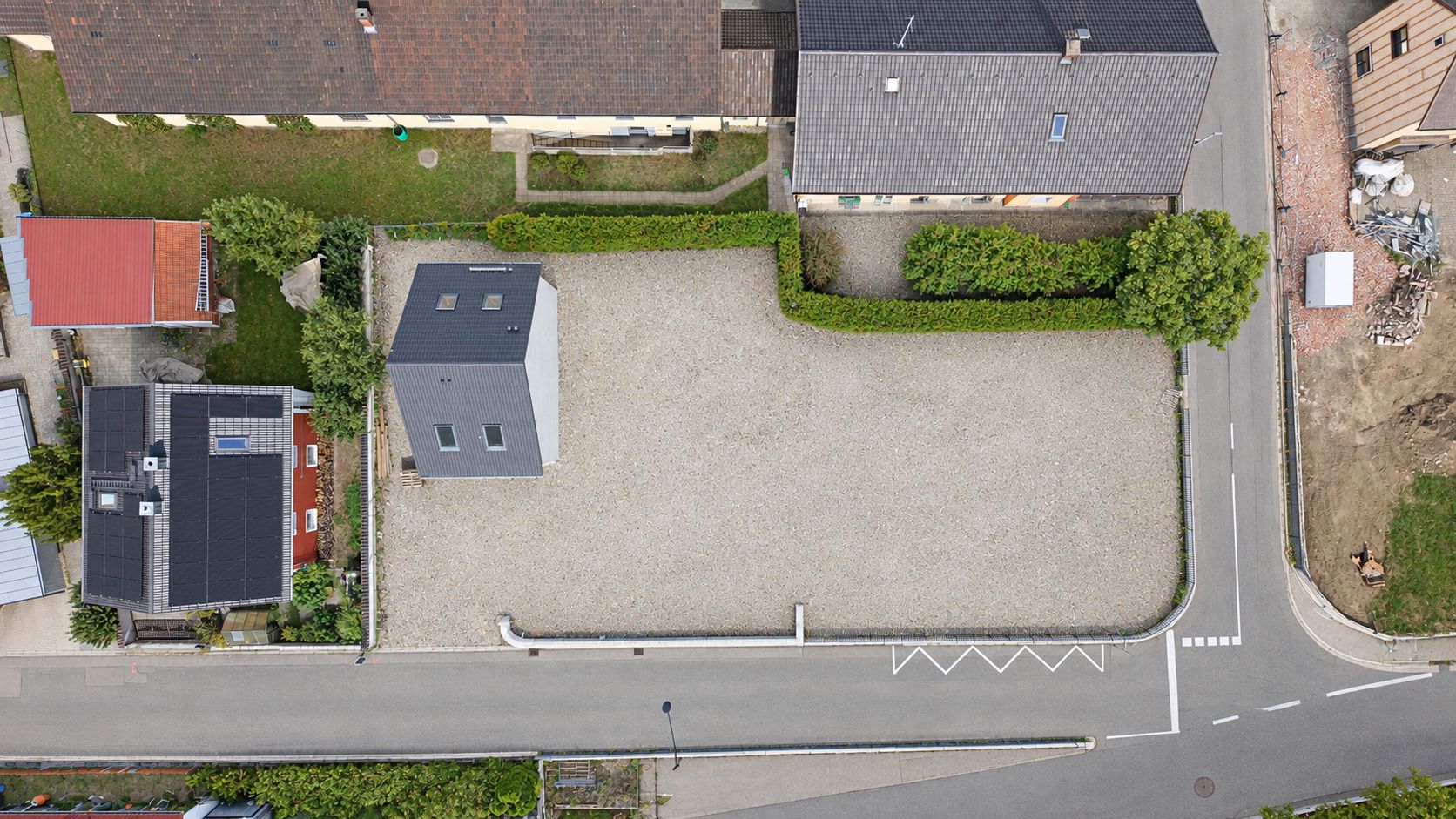 Luftaufnahme eines Wohnhauses mit einem großen, offenen Kiesplatz und angrenzenden Straßen.
