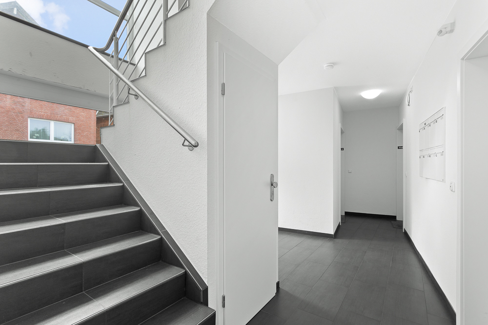 Heller Flur mit dunklem Fliesenboden, Treppe und Briefkästen an der Wand.