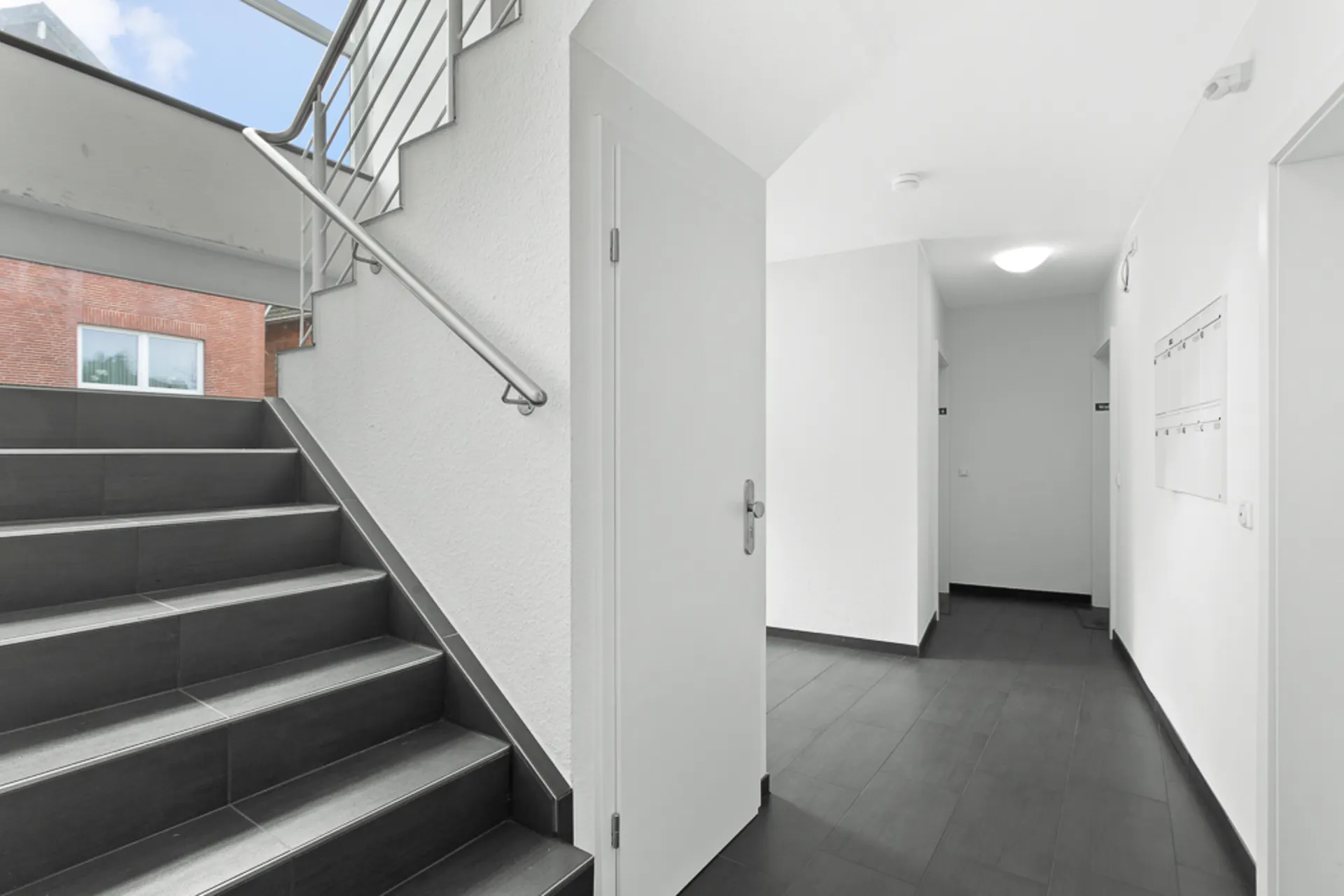 Heller Flur mit dunklem Fliesenboden, Treppe und Briefkästen an der Wand.