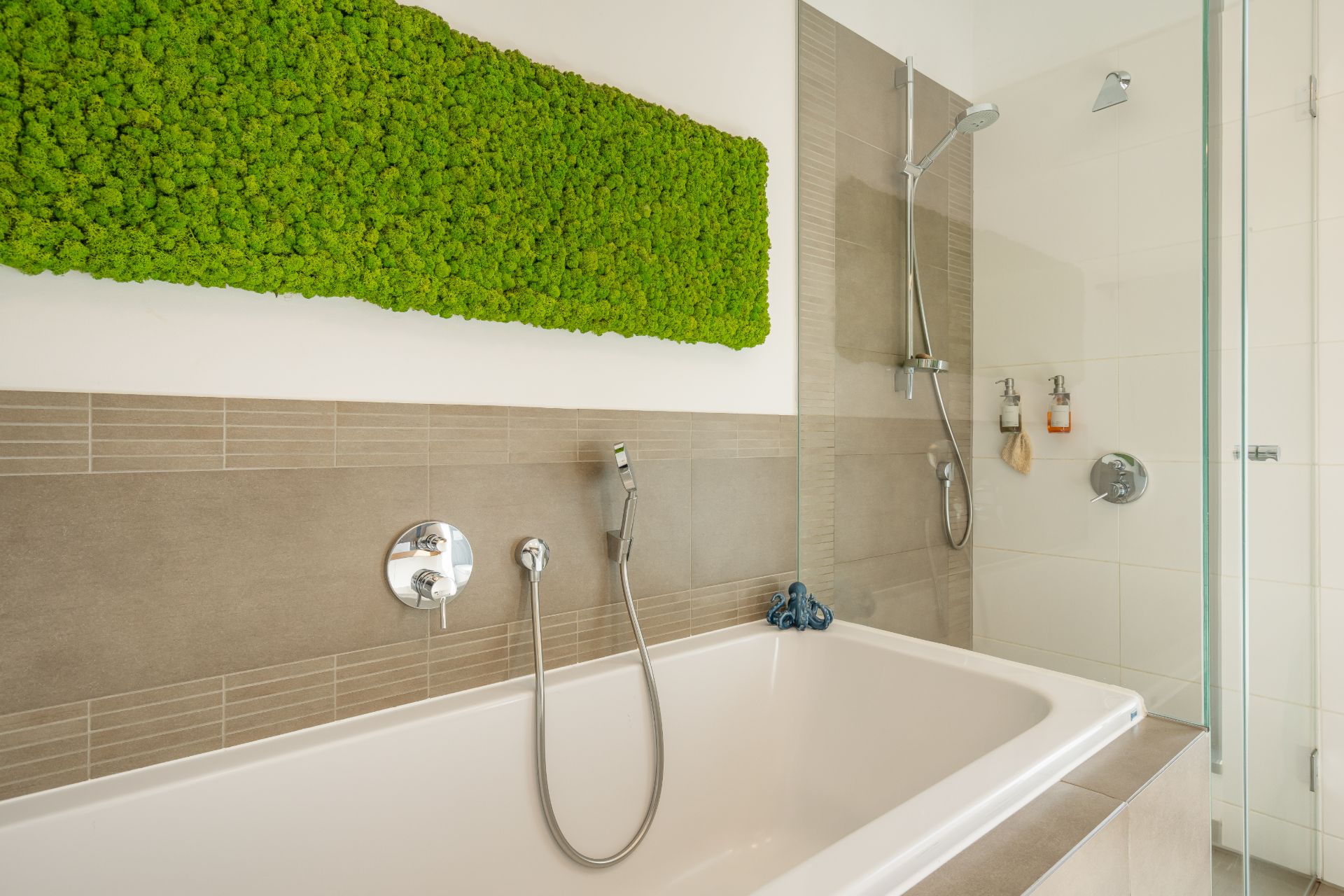 Modernes Badezimmer mit Badewanne, Dusche und grünem Moos-Deko an der Wand.