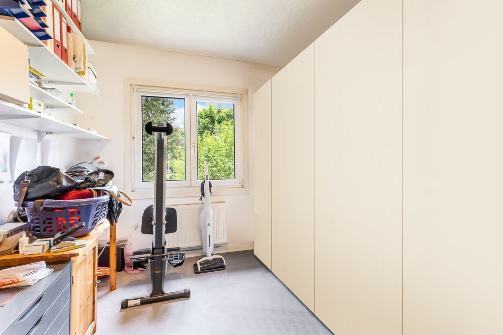 Heller Raum mit großem Schrank, Regal, Fitnessgerät und Fenster mit Blick ins Grüne.
