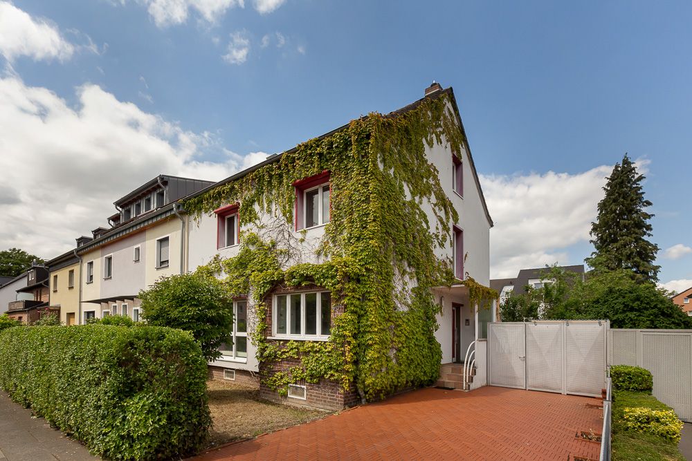Eckhaus mit Efeu bewachsener Fassade, rotem gepflastertem Hof und Hecke am Gehweg.