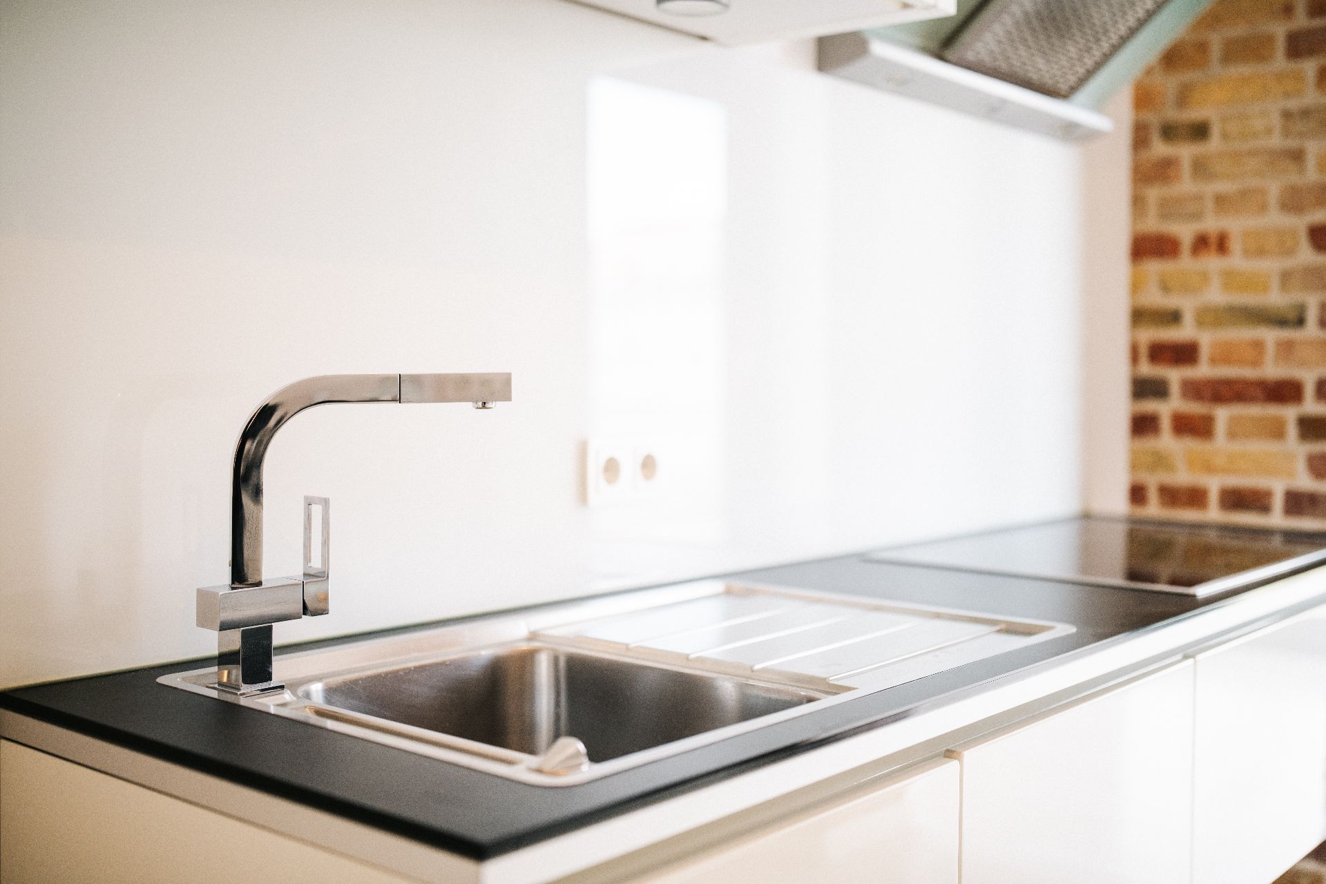 Moderne Küche mit Edelstahlspüle, Wasserhahn und Kochfeld auf heller Arbeitsplatte.