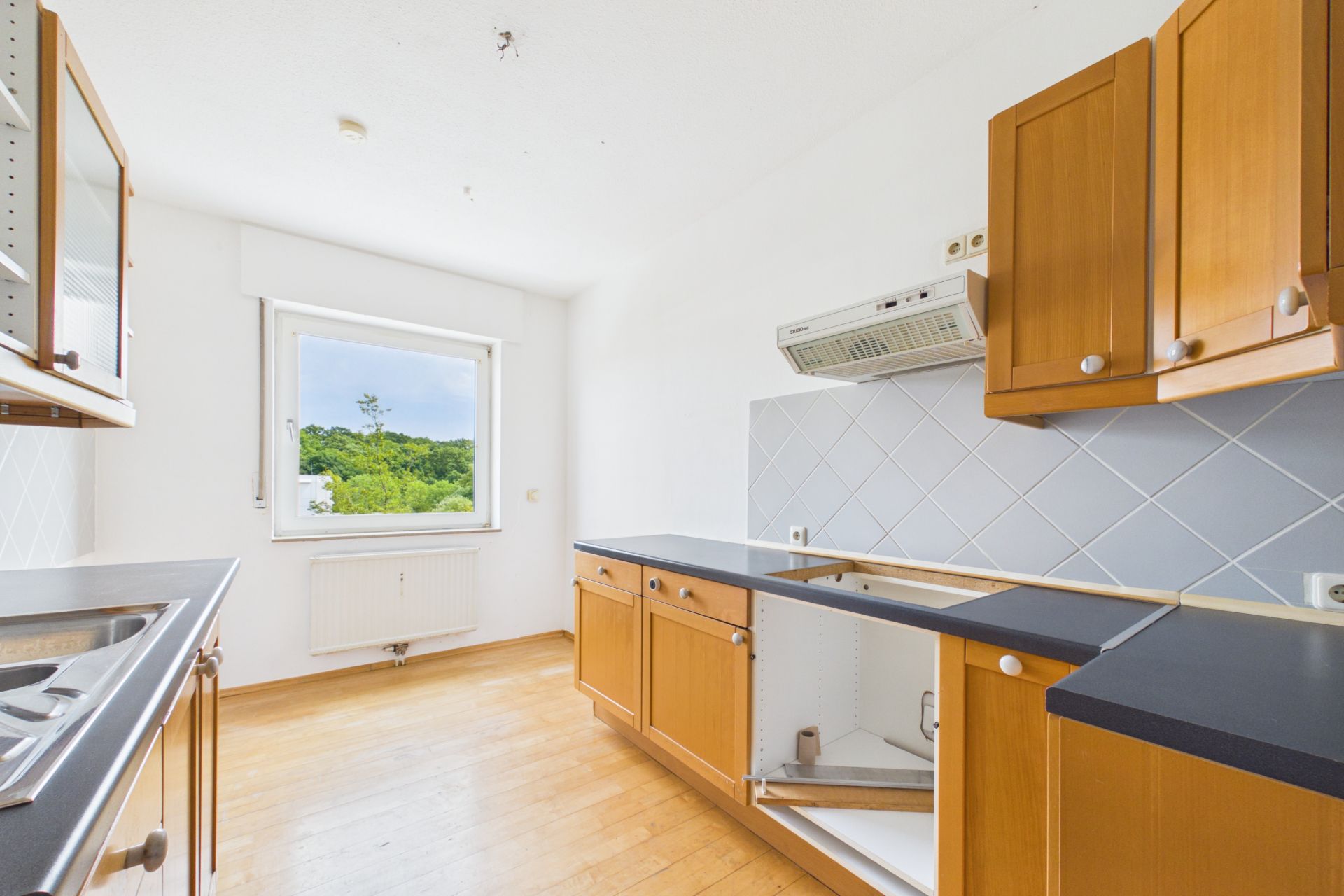Leere Küche mit Holzmöbeln, offenem Fenster und Blick ins Grüne.