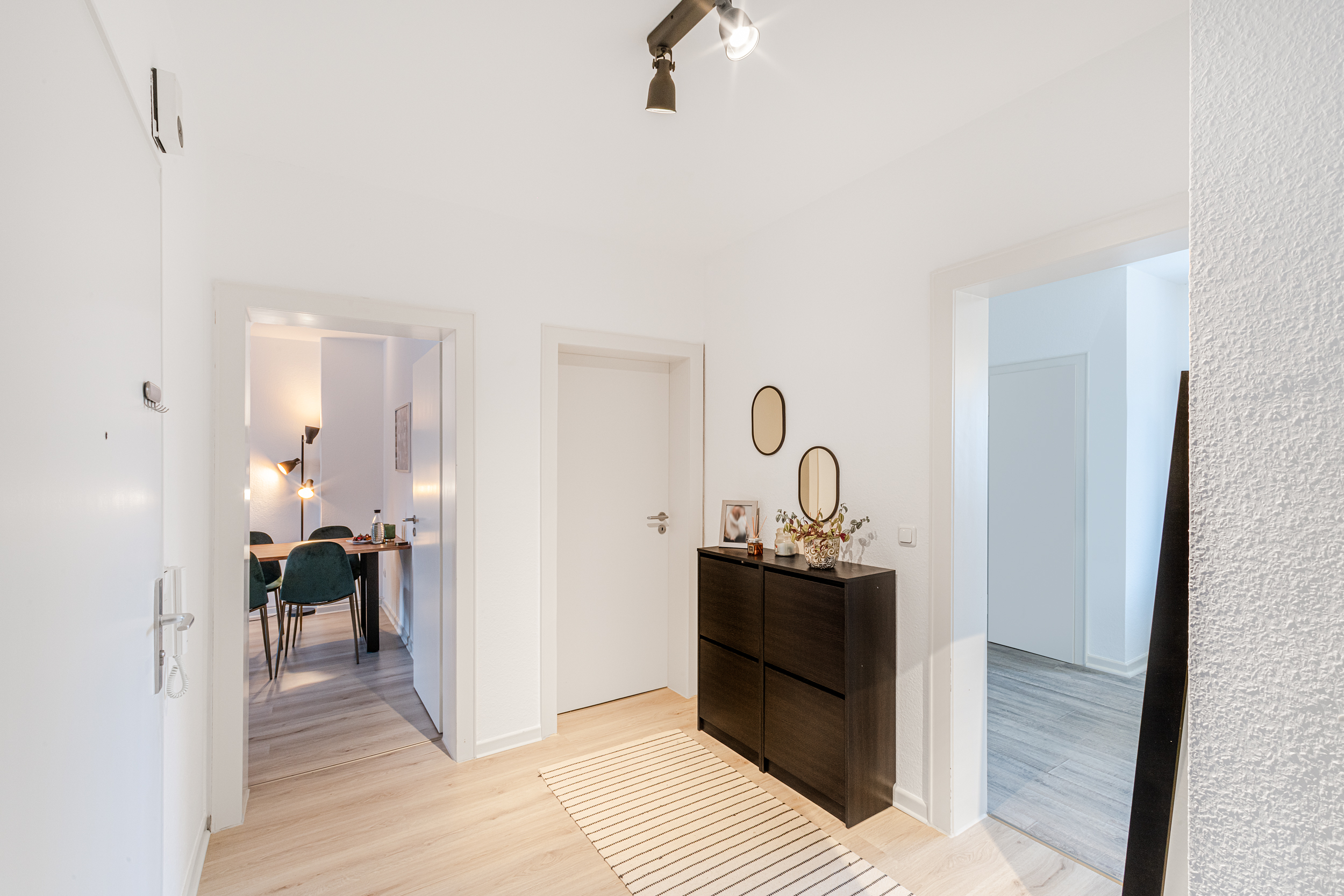 Heller Flur mit Kommode, zwei runden Spiegeln und Teppich, Türen führen in andere Räume.