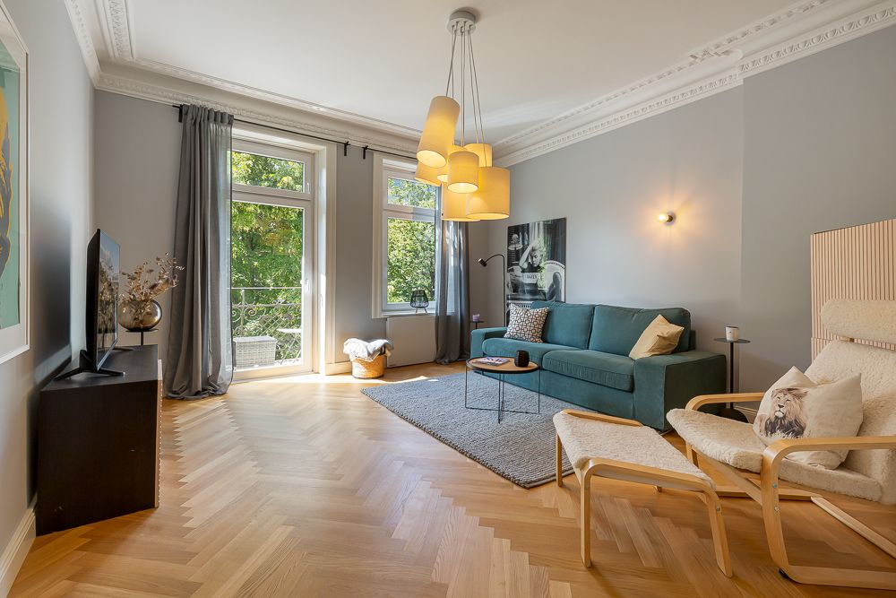 Helles Wohnzimmer mit Sofa, Sessel, Fernseher und großen Fenstern zum Garten.