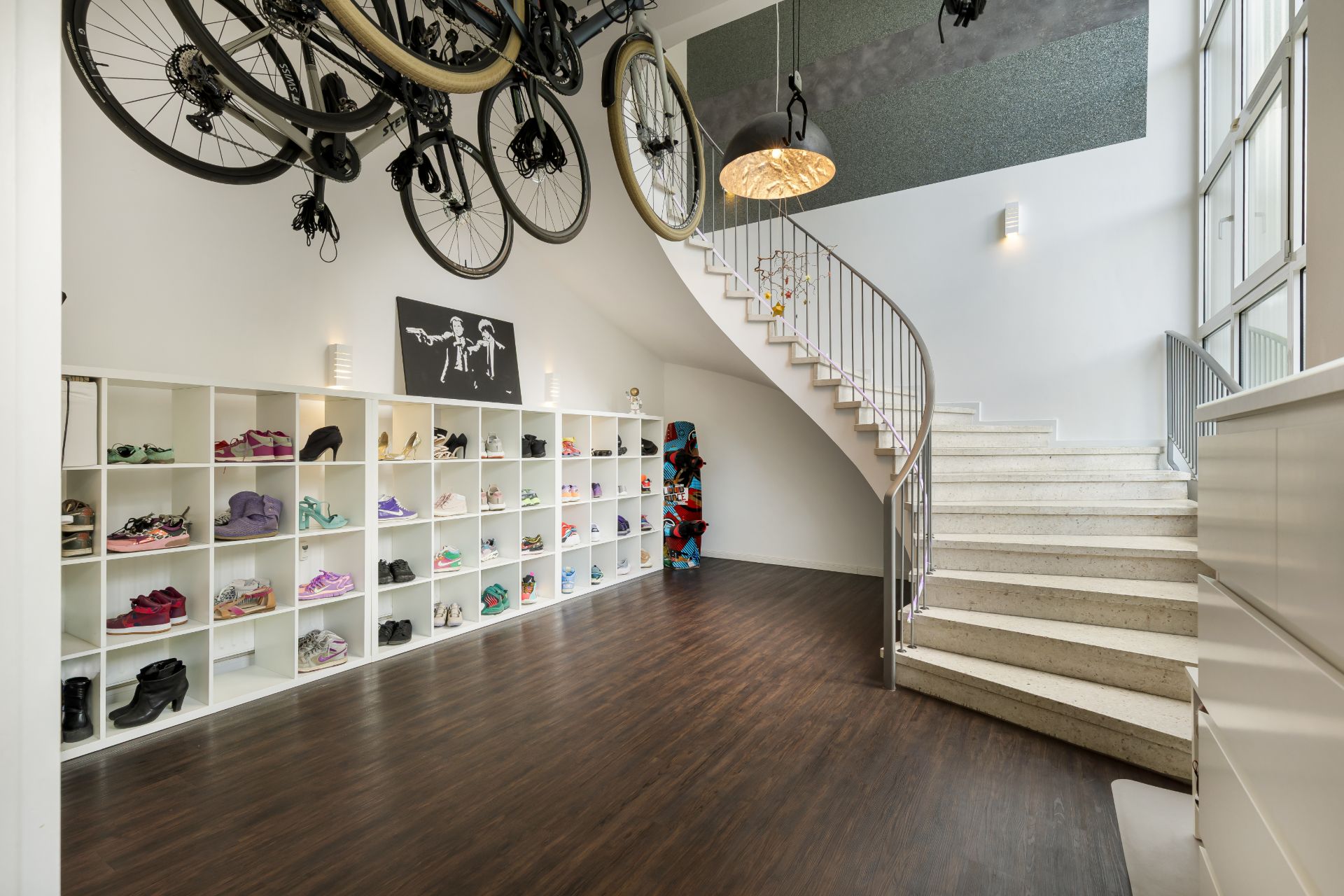 Moderner Flur mit Treppe, Wandregalen voller Schuhe und aufgehängten Fahrrädern an der Decke.