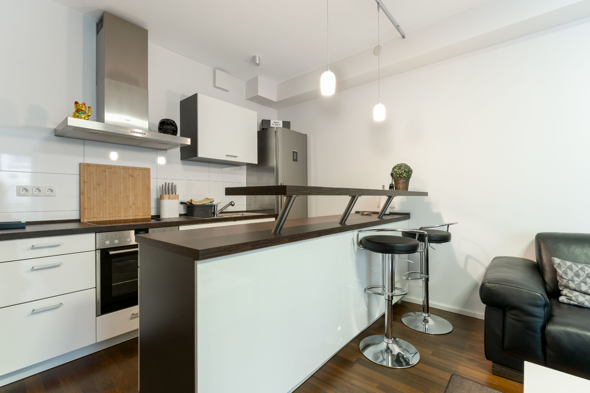 Moderne Küche mit Bartresen, zwei Hockern, Kühlschrank und Sofa auf Holzfußboden.