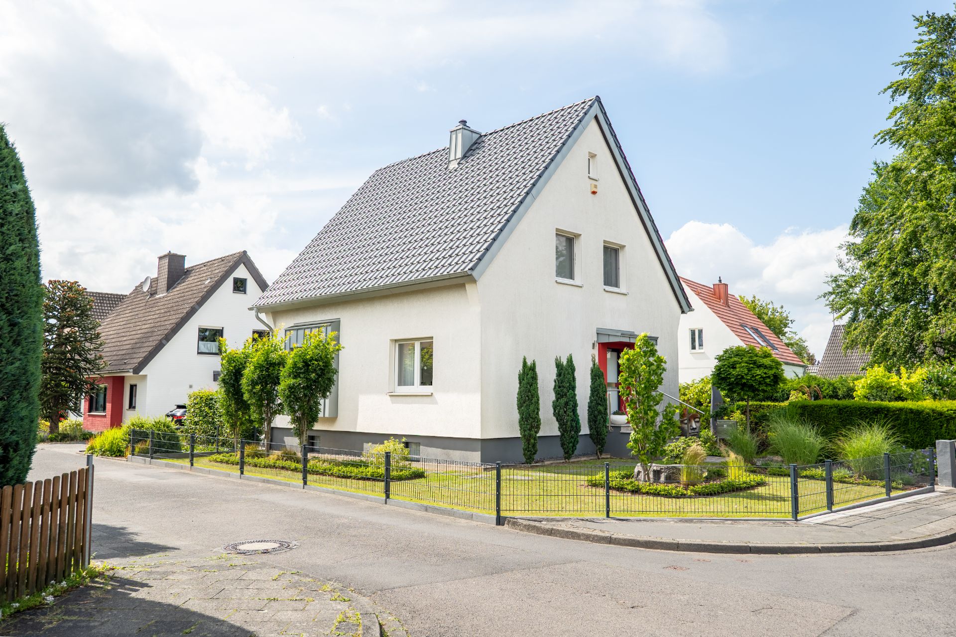 Weißes Einfamilienhaus mit Garten und Zaun an einer Straßenecke.