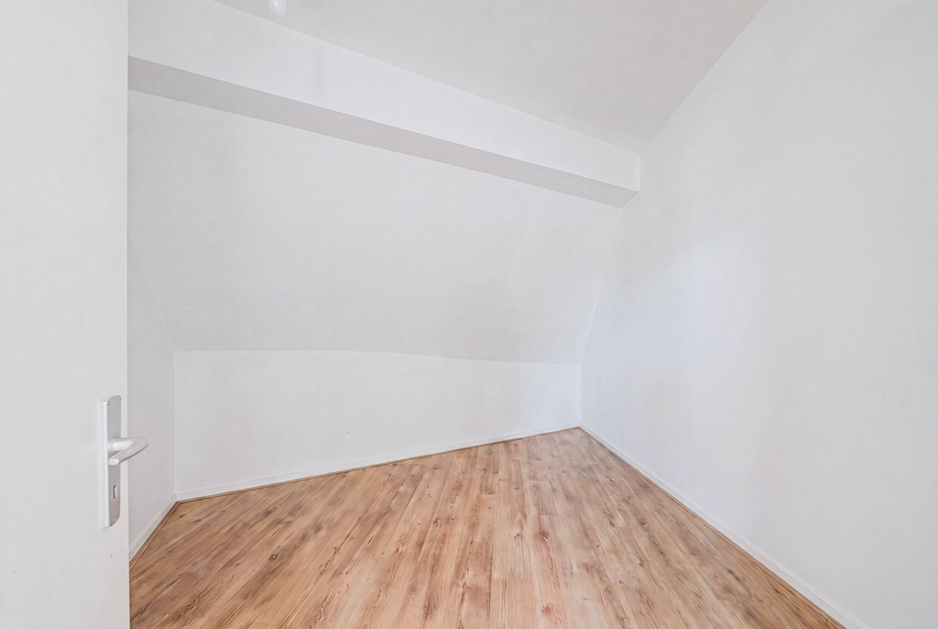 Leerer Raum mit weiß gestrichenen Wänden und Holzfußboden, Tür links geöffnet.