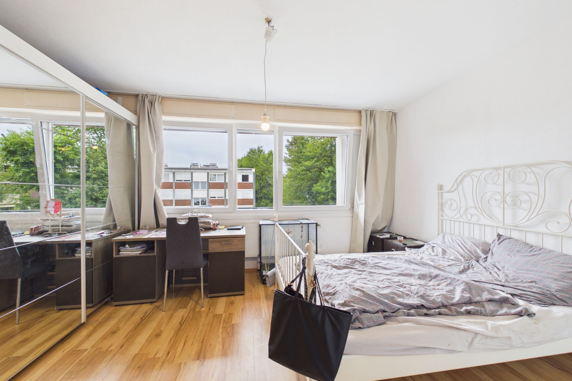 Helles Schlafzimmer mit Doppelbett, Schreibtisch, großem Fenster und Spiegel-Kleiderschrank.