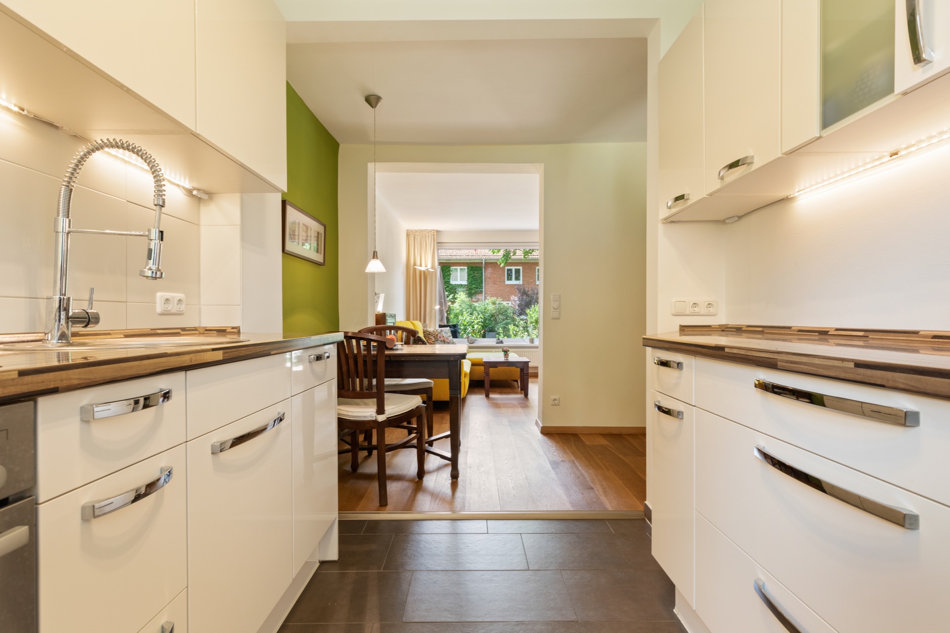 Helle Küche mit modernen Schränken, Blick ins Ess- und Wohnzimmer mit Holzboden.