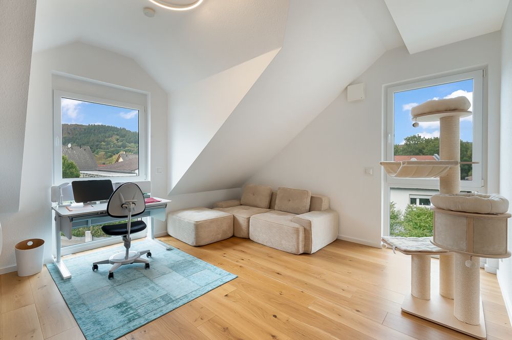 Helles Zimmer mit Schreibtisch, Stuhl, Sofa und Kratzbaum auf Holzfußboden.