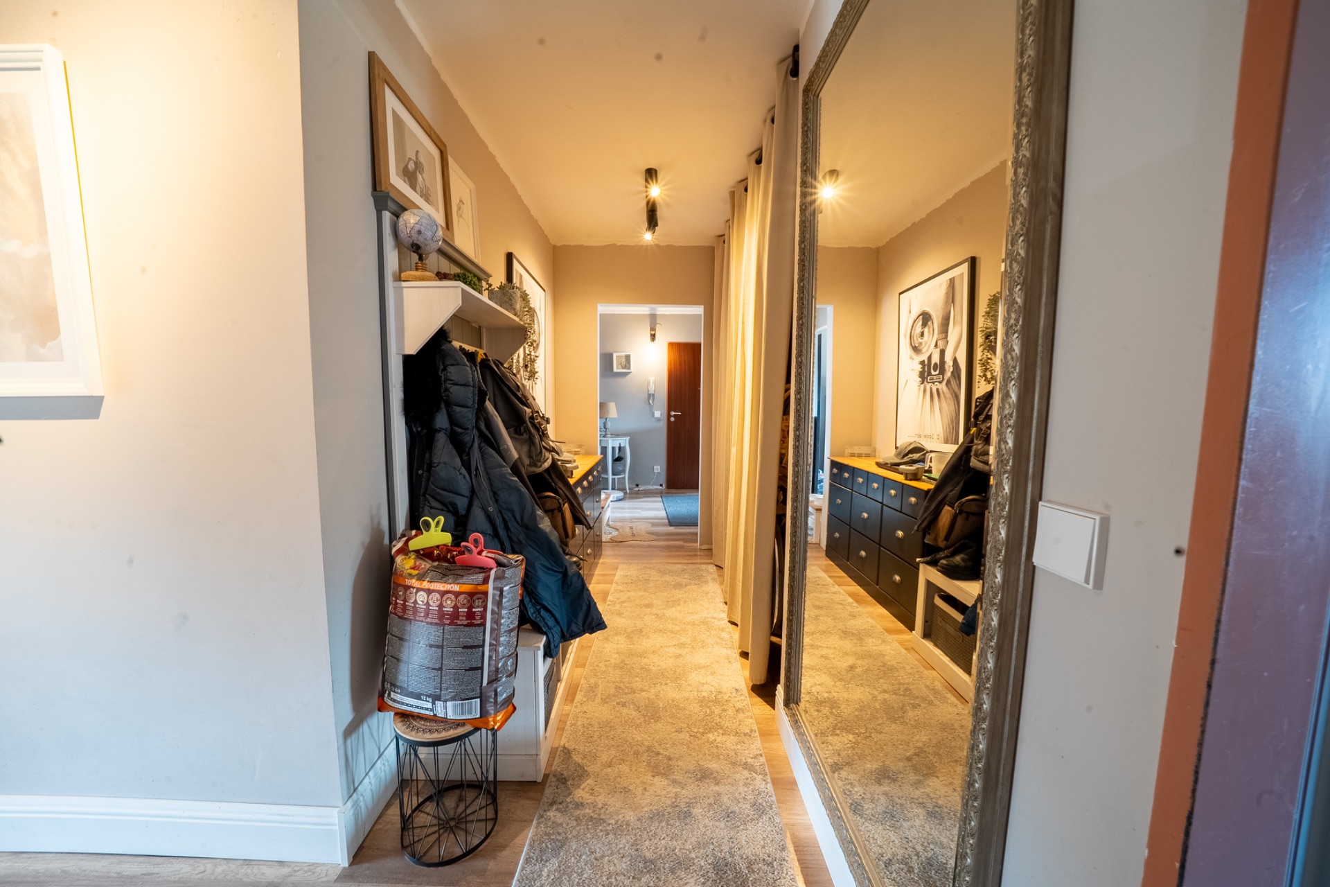 Flur mit Garderobe, großem Spiegel, Kommode und Teppich in einer Wohnung.