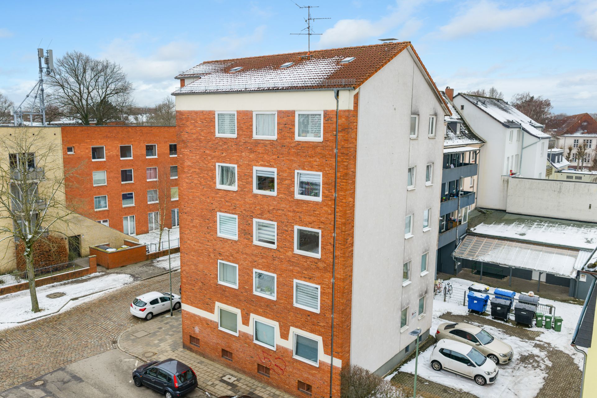 Mehrstöckiges Wohngebäude mit roter Klinkerfassade und Schneeresten auf dem Dach.