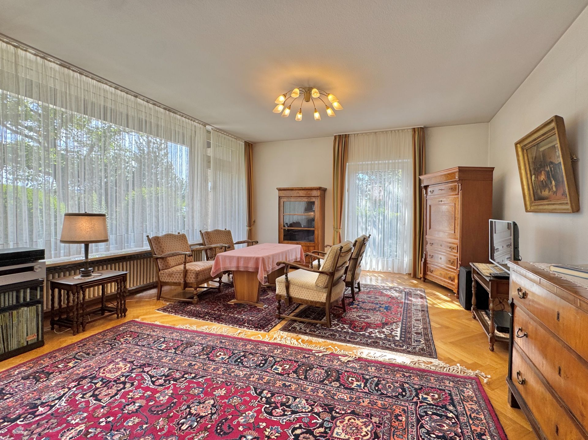 Helles Wohnzimmer mit großen Fenstern, Teppich, Holzmöbeln und Esstisch.